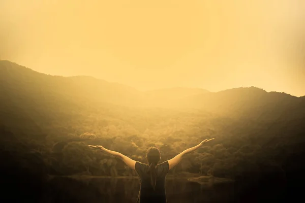 Silhouette of woman on a summit with upraised arms on the top mountain with the sunset, Praise for GOD.