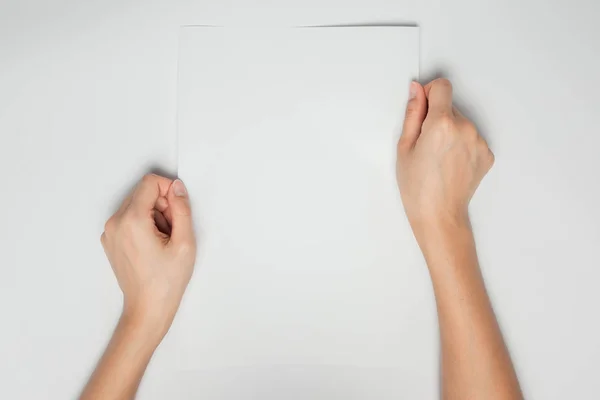 Uma mão feminina segura um papel branco vazio isolado em fundo branco — Fotografia de Stock