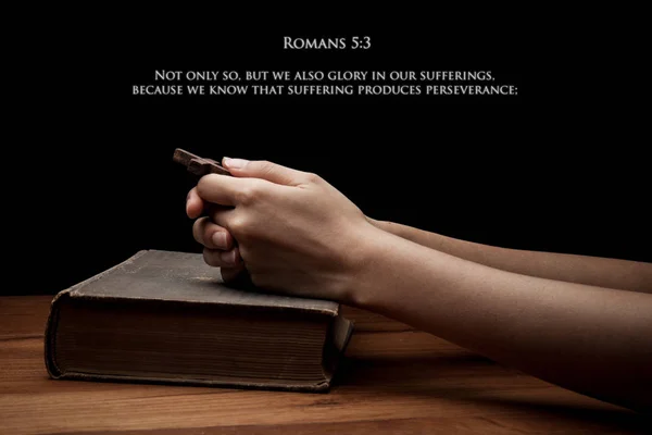 Hands holding a cross on holy Bible with verse Romans 5:3 — Stock Photo, Image