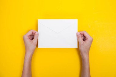 Bir kadın el sarı arka plan üzerinde bir zarf ve kartpostal tutun