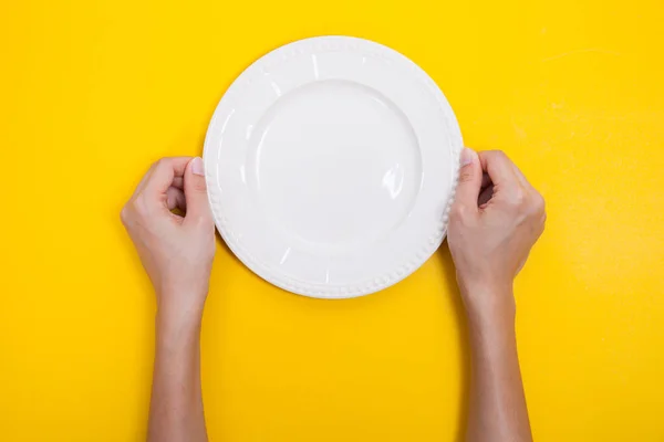 Женщина две руки держать белое блюдо на желтом фоне — стоковое фото