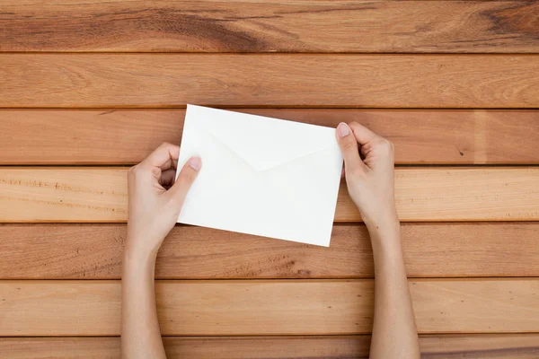 Main de femme tenir une enveloppe et une carte postale sur le bureau en bois , — Photo