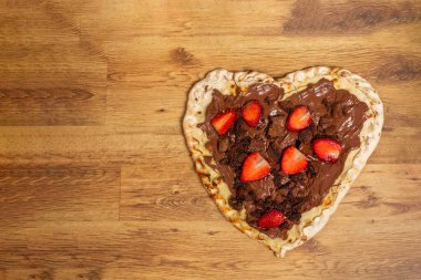 Kalp şeklinde pizza, çilekli çikolata aromalı ve ahşap arka planda Sevgililer Günü için browni. Tatlı pizza. Mesaj için yer var. Üst görünüm, alanı kopyala.