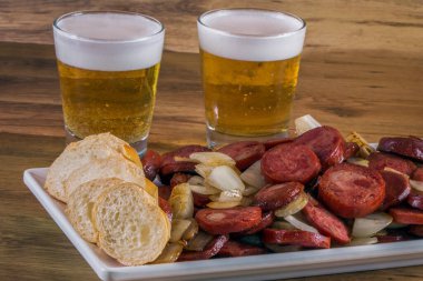 Ekmek ve soğanlı füme sosis ve ahşap arka planda bir bardak bira. Atıştırmalık meze, sosis ve soğan.