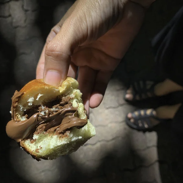 woman\'s hand holding donut stuffed with chocolate.