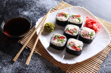 Beyaz tabakta porsiyon suşi ruloları, wasabi, zencefil, soya sosu, ahşap çubuklar. Japon yemeği..