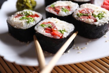 Beyaz tabakta porsiyon suşi ruloları, tahta yemek çubukları. Japon yemeği..