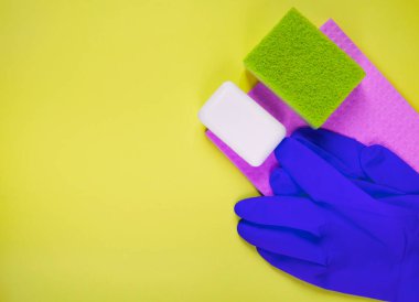 Sarı arka planda bez olan koruyucu eldivenler. Lastik eldivenler, süngerler ve sabun kalıbı manzarası. Fotokopi alanı olan temizlik şirketi için reklam afişi. 
