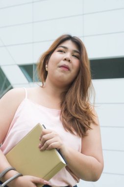 Asyalı güzel gülen yüzü şişman kadın poz ve holding kitapçık binanın ön portresi. 