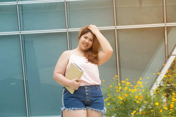 stock image Portrait of Asian pretty smiley face fat woman pose and holding booklet front of building. 