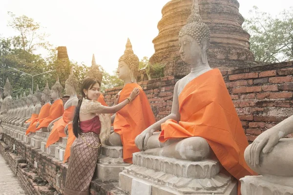古代タイの寺院で仏像のオレンジ色のローブを置く伝統的なアジアの女性のドレスします — ストック写真