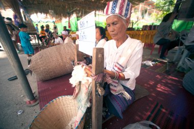 Phayao, Tayland-Mayıs 9,2015: Tanımlanamayan Tai Lue azınlık kadın kıdemli bir iplik geleneksel pamuk ipliği izleri Festivali şaşırtıcı 8 etnik gösterilen ahşap yapılmış antik haddeleme makine tarafından olduğunu.