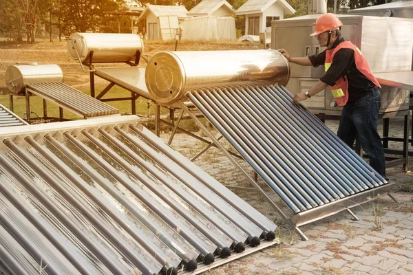 Der Arbeiter in Uniform und Helm kontrolliert konzentrierende Solarenergie mit Flachkollektor und Vakuumröhrenkollektor. — Stockfoto