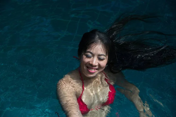 Pretty Asian woman wearing red bikini swimming at swimming pool.