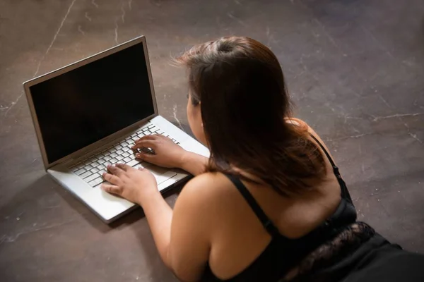 Asiatico plus size sexy, grasso e sovrappeso capelli lunghi modello femminile in abiti neri su marrone studio sfondo posa mentire uso laptop . — Foto Stock