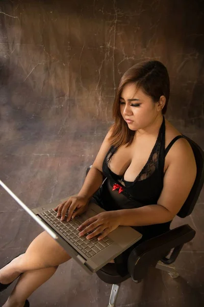 Asiática más tamaño sexy, gorda y con sobrepeso modelo de pelo largo femenino en vestidos negros en marrón estudio pose sentado uso portátil . — Foto de Stock