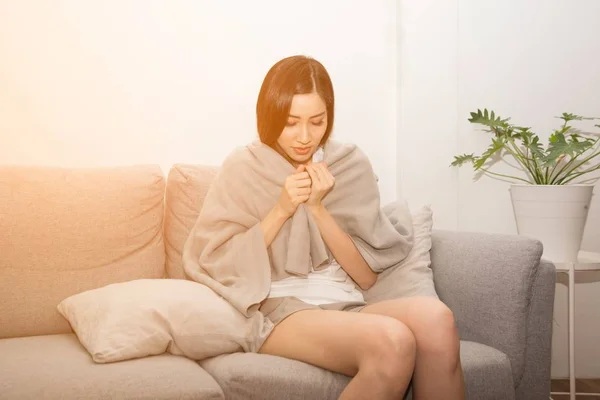 Asiática mujer triste sufriendo de frío debido a la fiebre en el sofá en la habitación . —  Fotos de Stock