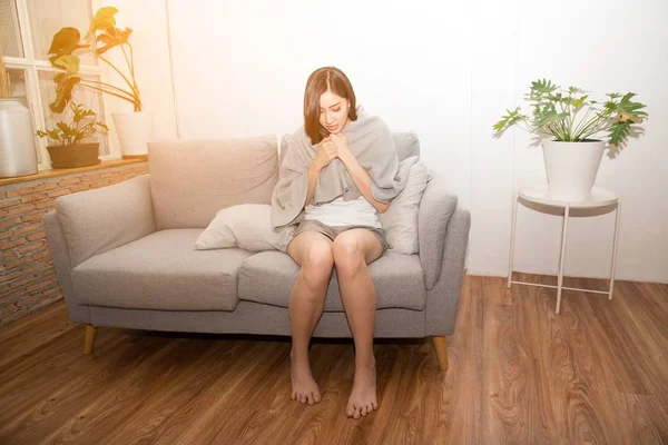 Ασιάτης/ισσα γυναίκα λυπημένος υποφέρει από κρύο λόγω πυρετό στον καναπέ στο δωμάτιο. — Φωτογραφία Αρχείου