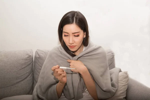 Asian woman sick from cold and used with thermometer suffering on sofa in the room.