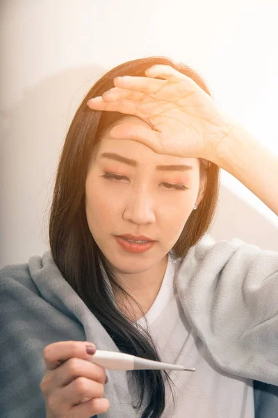 Aziatische vrouw ziek van koud en gebruikt met thermometer lijden op de Bank in de kamer. — Stockfoto