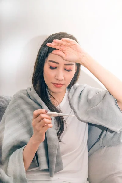 Aziatische vrouw ziek van koud en gebruikt met thermometer lijden op de Bank in de kamer. — Stockfoto