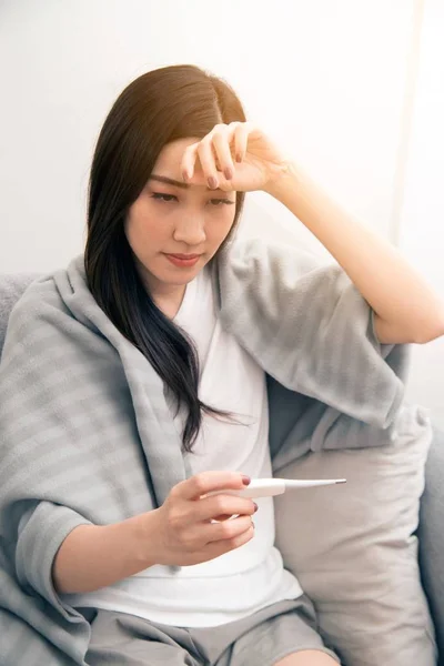 Asiatin an Erkältung erkrankt und mit Thermometer auf Sofa im Zimmer. — Stockfoto