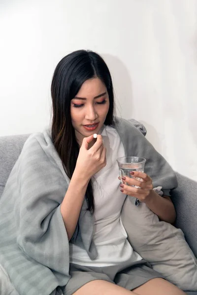 Asiático jovem mulher envolto em um cobertor e durante a doença e tomar antipiréticos . — Fotografia de Stock