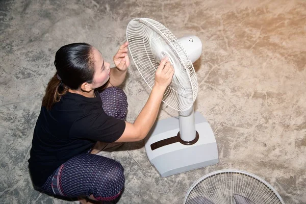 The housekeeper is assembling and installing an electric fan after cleaning.