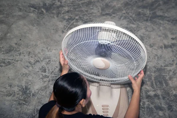 The housekeeper is assembling and installing an electric fan after cleaning.