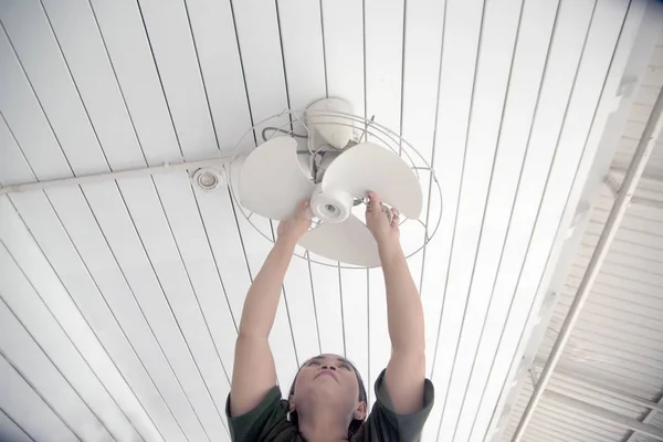 The housekeeper is installing the ceiling fan after being cleaned.