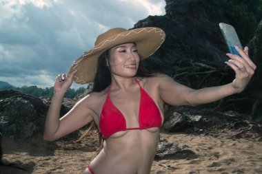 Bir cep telefonu mayo asyalı bir kadın kendini pozlar, o sahilde bir akıllı telefon ile selfie alıyor.