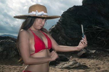 Bir cep telefonu mayo asyalı bir kadın kendini pozlar, o sahilde bir akıllı telefon ile selfie alıyor.