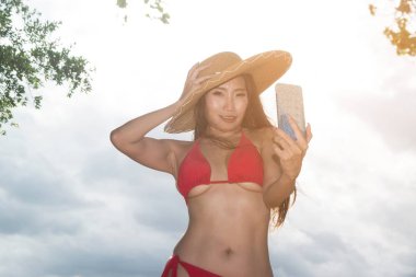 Bir cep telefonu mayo asyalı bir kadın kendini pozlar, o sahilde bir akıllı telefon ile selfie alıyor.