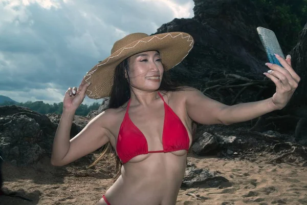 Bir cep telefonu mayo asyalı bir kadın kendini pozlar, o sahilde bir akıllı telefon ile selfie alıyor.