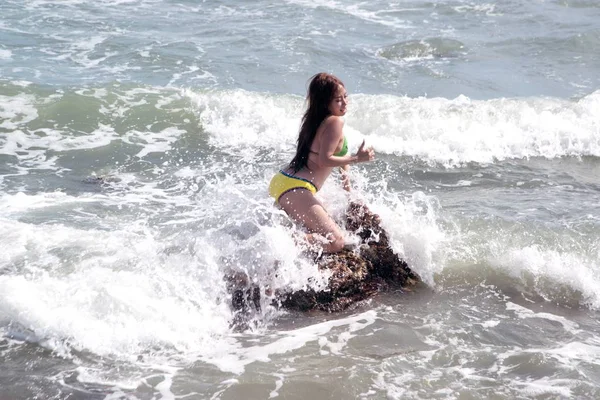 Uma mulher asiática em um maiô está sentada em uma rocha quando tem ondas fortes . — Fotografia de Stock