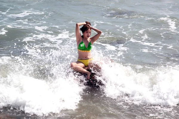 Uma mulher asiática em um maiô está sentada em uma rocha quando tem ondas fortes . — Fotografia de Stock