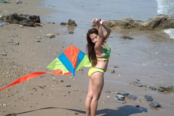 水着を着たアジアの女性は楽しみのためにカラフルな凧を演奏しています. — ストック写真