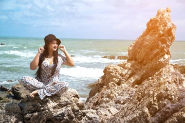 Asya artı boyutu şişman ve kilolu kadın beyaz elbiseler plajda kaya üzerinde oturan. 