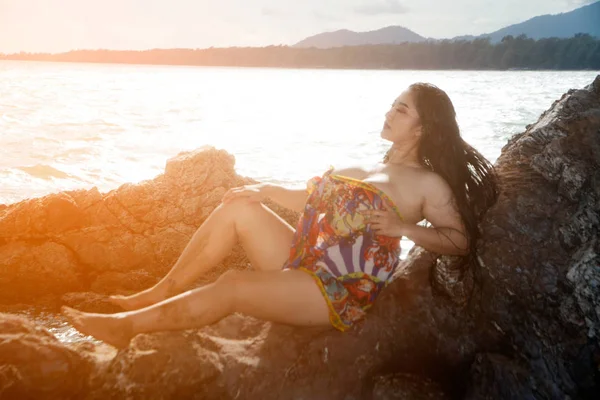Asiatische plus size dicke und übergewichtige Frau im Badeanzug liegt auf einem Rücken auf einem Felsen und starke Wellen am Strand. — Stockfoto