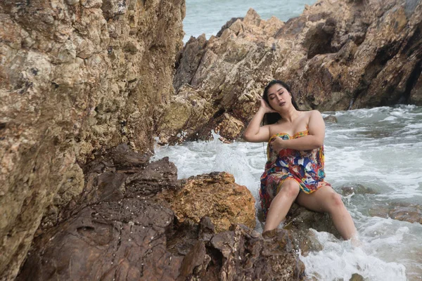 Asya artı boyutu şişman ve kilolu kadın bir yüzme elbisesi içinde kaya ve plajda güçlü dalgalar üzerinde oturan. — Stok fotoğraf