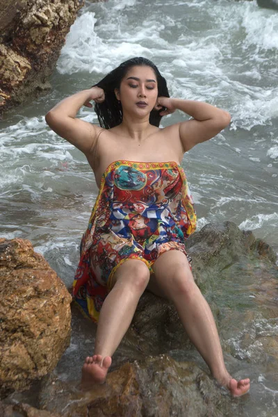 Asiatiska Plus storlek fett och överviktiga kvinna i en baddräkt sitter på Rock och starka vågor på stranden. — Stockfoto