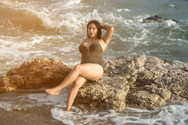 Asiática más tamaño gordo y mujer con sobrepeso en un traje de baño sentado en la roca y fuertes olas en la playa . — Foto de Stock