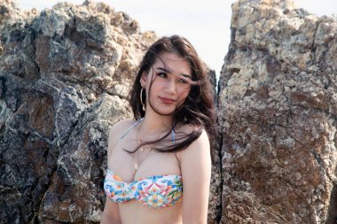 Sahilde bir kaya üzerinde duran beyaz bir mayo içinde güzel Asyalı kadın portresi. 