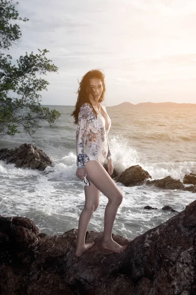 Retrato da bela mulher asiática em um maiô branco fica debaixo de uma árvore na praia . — Fotografia de Stock