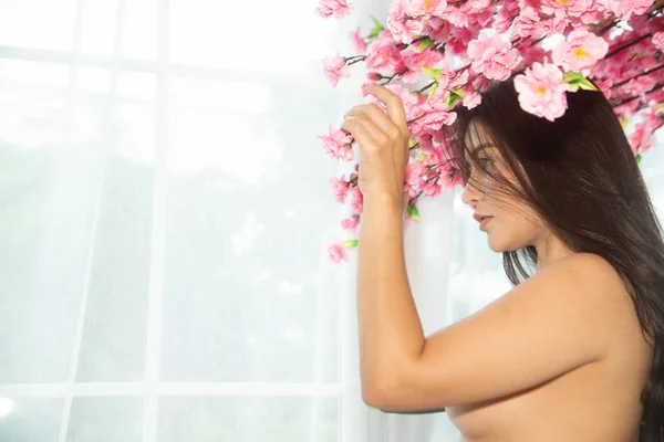 Sensual pretty sexy dresses Asian women sensuality standing under pink flower tree near window. — Stock Photo, Image