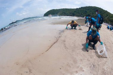 RAYONG, THAILAND-FEBRUARY 8. 2013: Tayland 'da Khao Laem Ya-Mo Ko samet Ulusal Parkı' ndaki Prew sahilindeki büyük bir plastik torba içinde ham petrolle kumu küreyen tanımlanamayan işçiler ve gönüllüler.