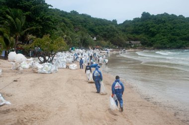 RAYONG, THAILAND-FEBRUARY 8. 2013: Tayland 'da Khao Laem Ya-Mo Ko samet Ulusal Parkı' ndaki Prew sahilindeki büyük bir plastik torba içinde ham petrolle kumu küreyen tanımlanamayan işçiler ve gönüllüler.
