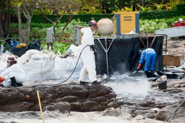RAYONG, THAILAND-FEBRUARY 8. 2013: Tayland 'daki Khao Laem Ya-Mo Samet Ulusal Parkı' ndaki Prew sahilindeki ham petrolün üzerine tanımlanamayan işçiler ve gönüllüler kimyasal püskürtüyor.