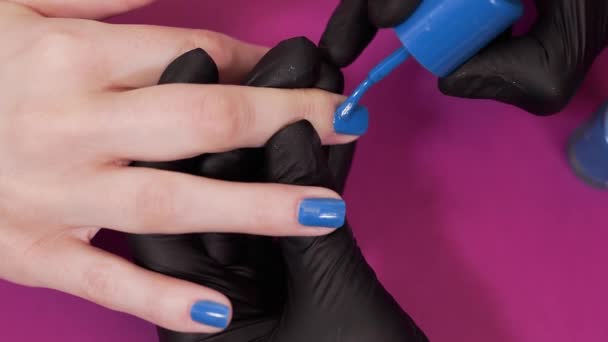 Маникюрша красит ногти клиентов синим оттенком лака — стоковое видео