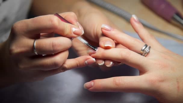 Maestro de manicura cubre las uñas de las mujeres por esmalte de uñas transparente — Vídeos de Stock
